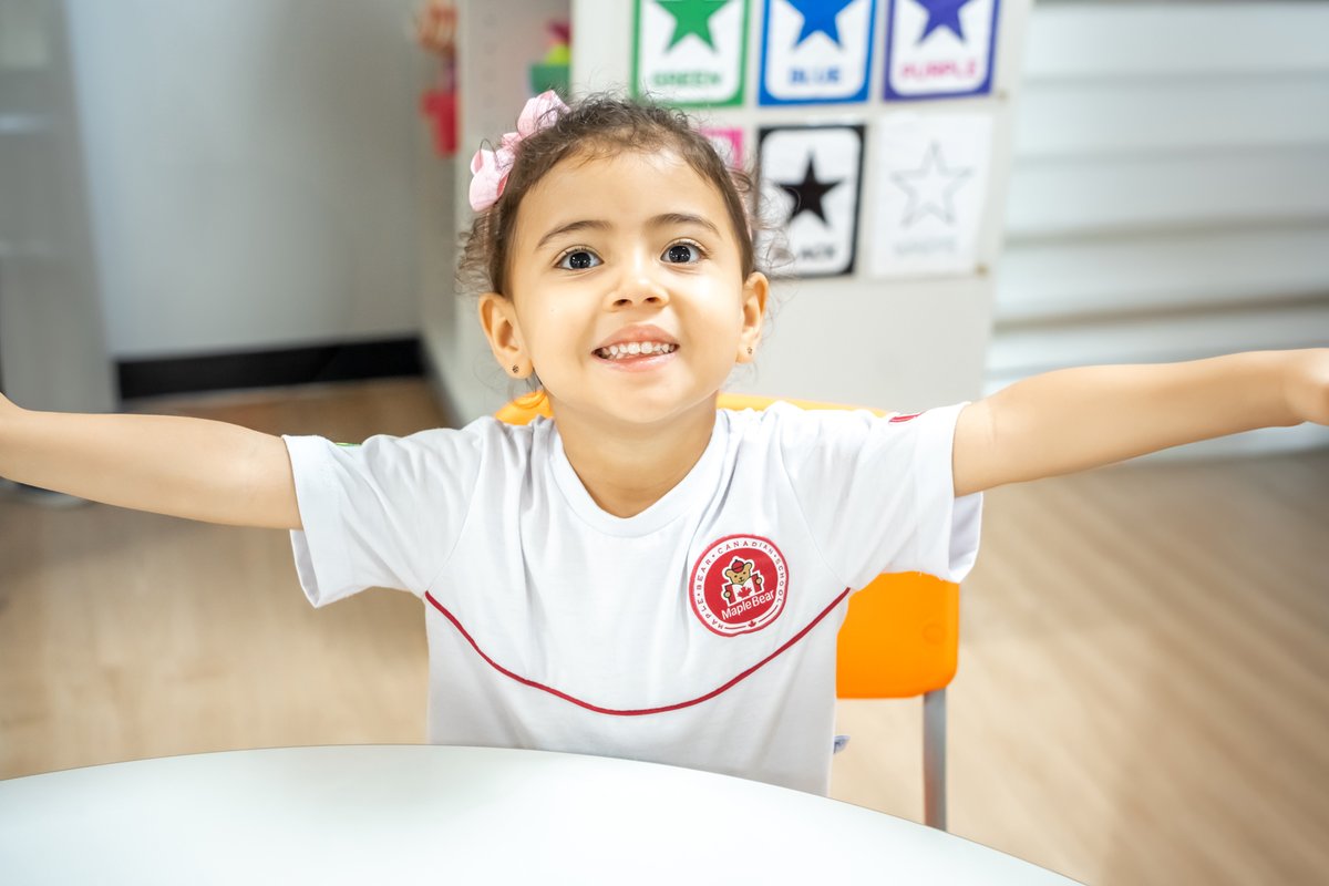 aluna da educação infantil de braços abertos dentro da sala de aula